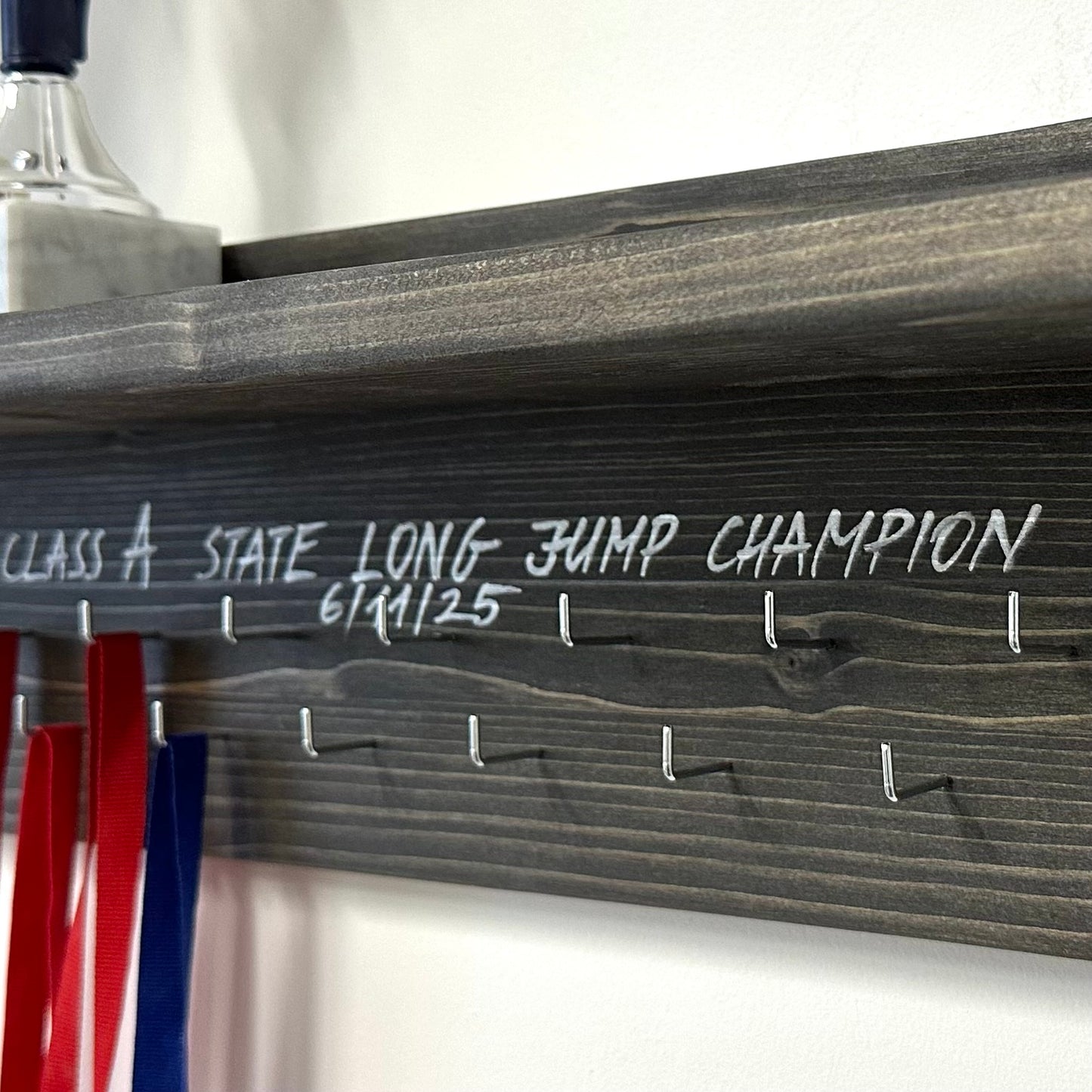 Pie sienas stiprināms medaļu turētājs ar trofeju plauktu un personalizētiem āķiem